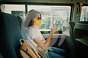 Hipster young girl in a protective mask on her face in a public transport bus with a smartphone in her hands