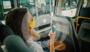 Hipster young girl in a protective mask on her face in a public transport bus with a smartphone in her hands