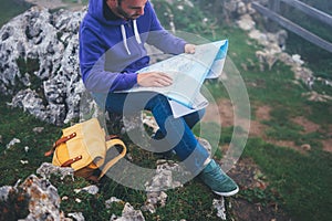 Hipster young man with backpack holding in hands and looking on map spain of foggy mountain, tourist traveler hiker on background