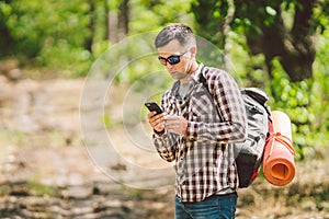 Hipster young man with backpack using smart phone on beautiful nature.Travel concept. Outdoor travel. Travel and explore