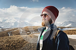 Hipster young man with beard and mustache wearing sunglasses posing against the background of mountains