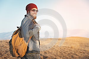 Hipster young man with beard and mustache wearing sunglasses posing against the background of mountains