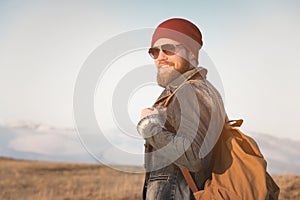 Hipster young man with beard and mustache wearing sunglasses posing against the background of mountains
