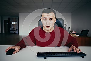 Hipster young man working in the office puzzled looks at the monitor of your computer. Interested in camera view