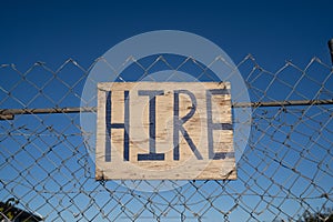 `Hire` sign on  fence with blue sky