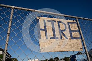 `Hire` sign on  fence with blue sky