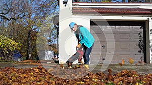 Hired female worker blowing leaves from garage entrance in autumn