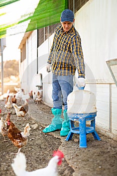 Hired male worker repairing chicken feeders in poultry farm