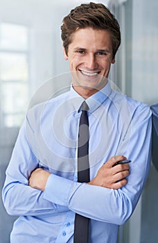 His attitude will take him far. A handsome young businessman crossing his arms and smiling at you.
