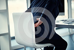 His back is carrying his workload. a businessman experiencing back ache while working at his desk.