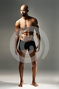 His body is perfectly chiselled. Studio shot of a sexy young man against a gray background in his underwear.