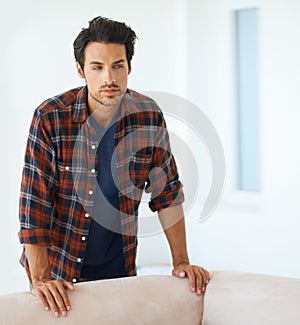 His brooding good looks will leave you breathless. a handsome young man standing behind the sofa at home.