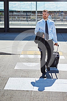 His career is about to take off. a professional businessman walking toward an airport with his luggage.