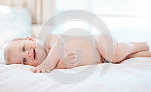 His giggles are true. an adorable little baby boy lying on a bed at home.