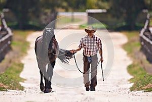 His horse is his best friend. Rearview shot of a cowboy leading his horse by the reins.