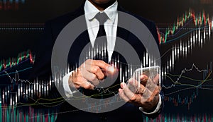 On his left hand, a man in a suit holds a cell phone. His right hand is pointing to a rapidly expanding stock chart. backdrop and