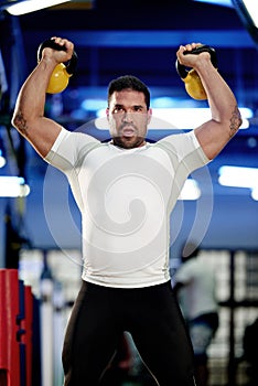 His muscles mean business. a man working out with kettle bells at the gym.