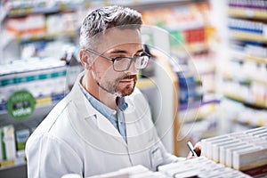 His stock keeps customers coming back. a mature pharmacist doing inventory in a pharmacy.