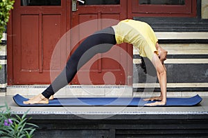 On his terrace, a young Asian girl with a stunning appearance is practicing Yoga while sporting a short haircut, a yellow shirt,