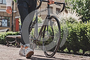 On his way. Close up of young man standing in the park with a bicycle