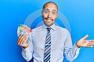 Hispanic adult business man holding swiss franc banknotes celebrating achievement with happy smile and winner expression with