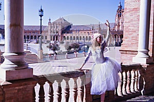 Hispanic adult female classical ballet dancer in white tutu and pink cancer fight scarf making figures leaning on a stone railing
