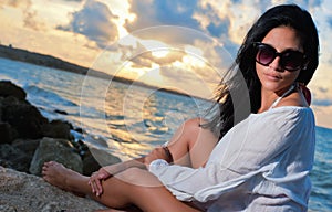 Hispanic beauty sitting by the ocean at sunset