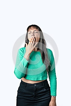 Hispanic brunette woman yawning and covering her mouth with hand on white background