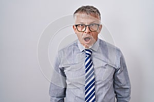 Hispanic business man with grey hair wearing glasses afraid and shocked with surprise and amazed expression, fear and excited face