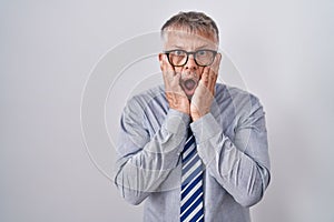 Hispanic business man with grey hair wearing glasses afraid and shocked, surprise and amazed expression with hands on face