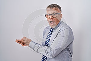 Hispanic business man with grey hair wearing glasses pointing aside with hands open palms showing copy space, presenting