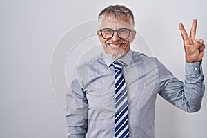 Hispanic business man with grey hair wearing glasses showing and pointing up with fingers number two while smiling confident and