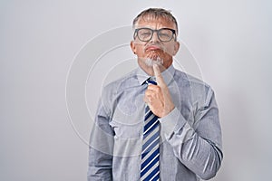 Hispanic business man with grey hair wearing glasses thinking concentrated about doubt with finger on chin and looking up
