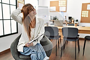 Hispanic business woman working at the office smiling confident touching hair with hand up gesture, posing attractive and