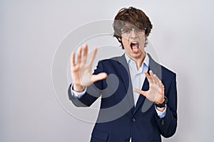 Hispanic business young man wearing glasses afraid and terrified with fear expression stop gesture with hands, shouting in shock