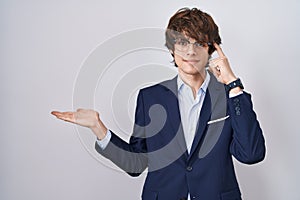 Hispanic business young man wearing glasses confused and annoyed with open palm showing copy space and pointing finger to forehead