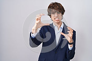 Hispanic business young man wearing glasses shouting frustrated with rage, hands trying to strangle, yelling mad