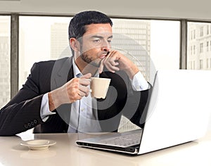 Hispanic businessman holding cup of coffee sitting at business district office desk working