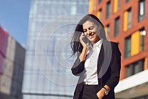 Hispanic businesswoman smiling speaks on a mobile outdoors