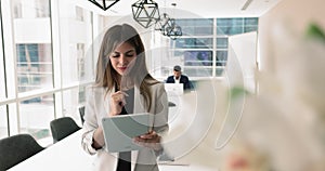 Hispanic businesswoman standing in modern boardroom working on her tablet