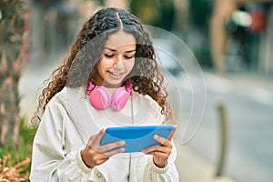 Hispanic child girl smiling happy using headphones and touchpad at the city