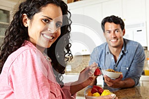 Hispanic couple eating cereal and fruit in kitchen