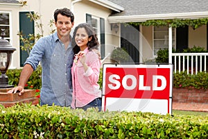 Hispanic couple outside home with sold sign