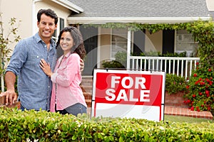 Hispanic couple satnding with a sign outside house