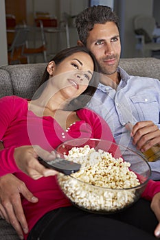 Hispanic Couple On Sofa Watching TV And Eating Popcorn