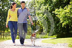 Hispanic Couple Taking Dog For Walk In Countryside