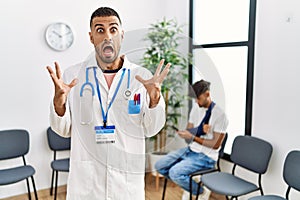 Hispanic doctor man at waiting room with pacient with arm injury celebrating victory with happy smile and winner expression with