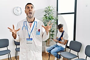 Hispanic doctor man at waiting room with pacient with arm injury crazy and mad shouting and yelling with aggressive expression and