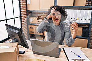 Hispanic doctor woman with curly hair standing by manikin at small business smiling happy doing ok sign with hand on eye looking