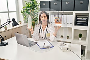 Hispanic doctor woman holding model of human anatomical skin and hair skeptic and nervous, frowning upset because of problem photo